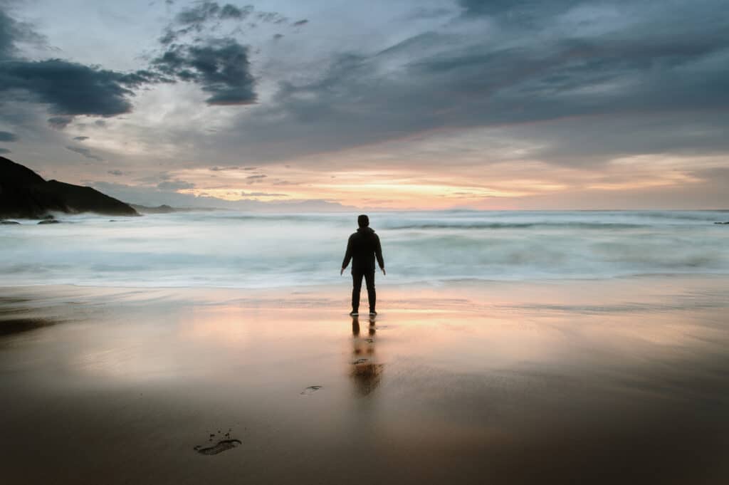 Mann som står på ei strand og ser utover.