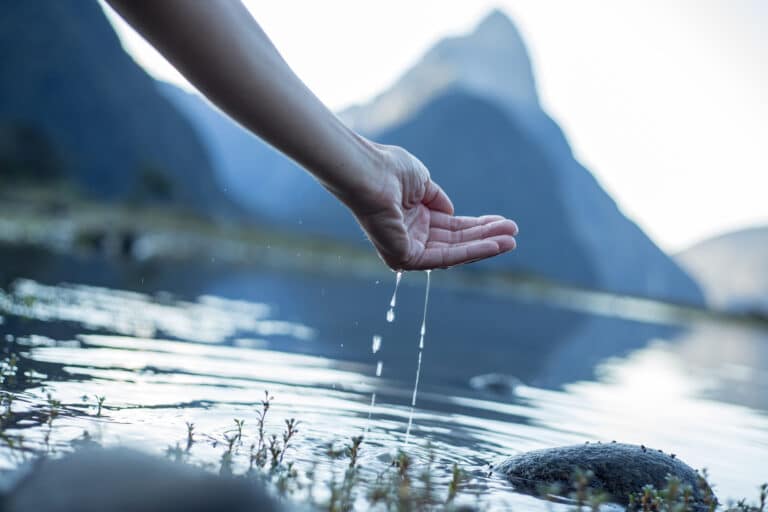 Kvinnehånd kjenner på vannet i en innsjø til fjells.