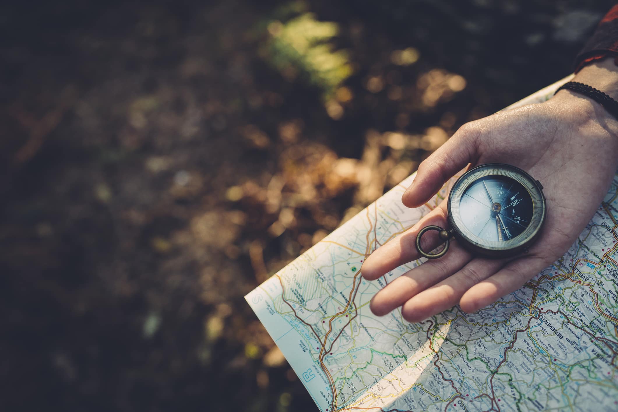 En person holder kart og kompass i hånden ute i naturen