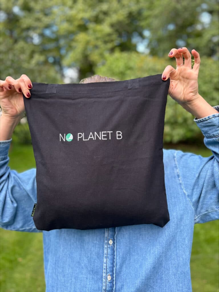 Holdet et svart svanemerket handlenett med "No Planet B" tekst foran fjeset